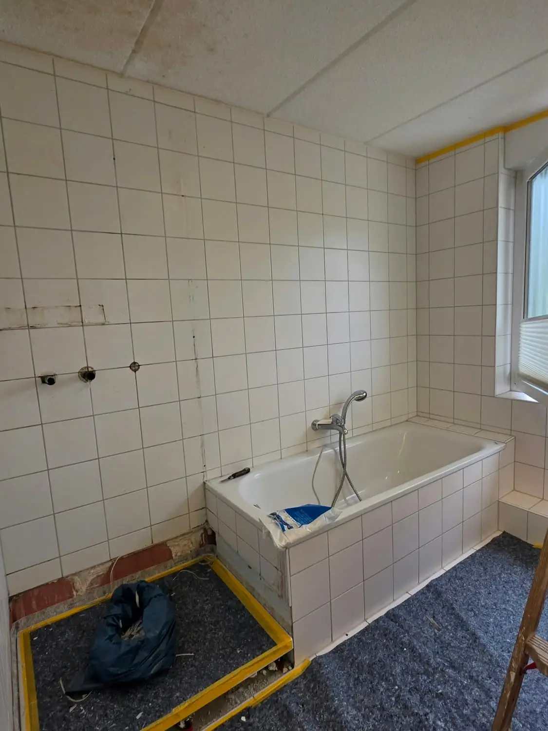 Badezimmer vor der Arbeit: weiß geflieste Wände, Duschwanne ausgebaut, Boden abgedeckt