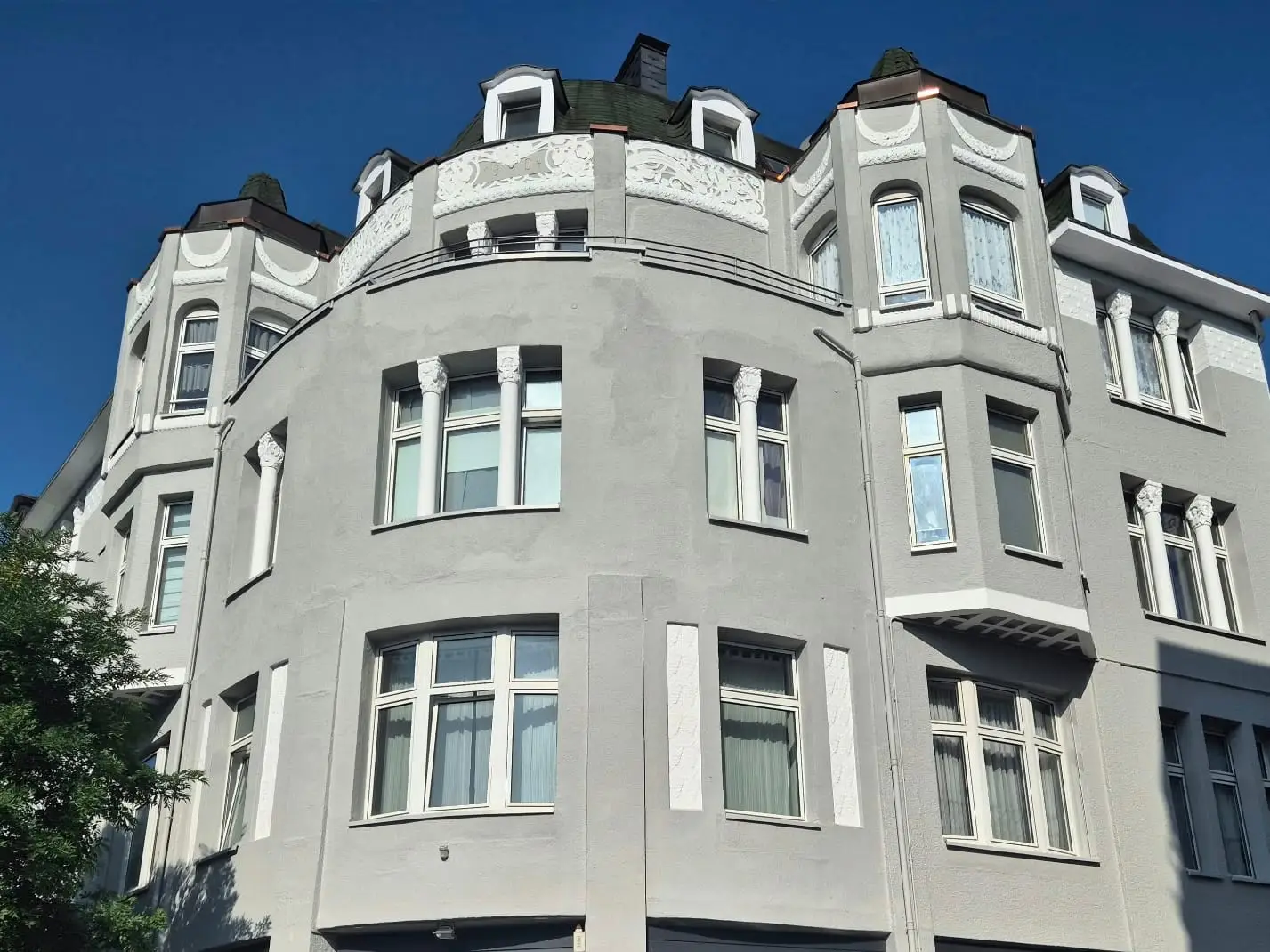 Das fertige Jugendstil-Eckhaus in Grau mit weißen Stuckelementen vor blauem Himmel