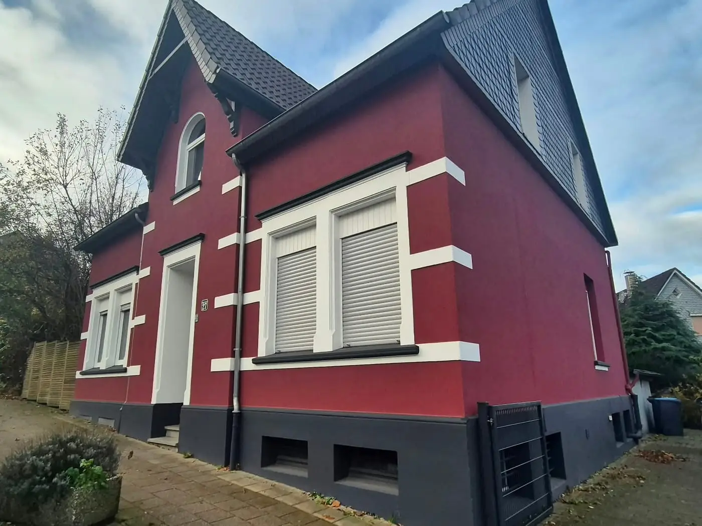 Frisch gestrichenes Wohnhaus in Weinrot mit weißen Fensterfaschen und anthrazitfarbenem Sockel