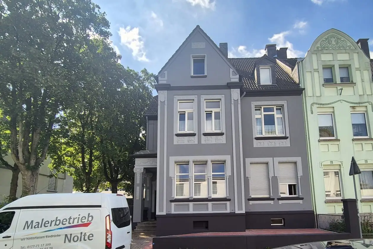 Fertig saniertes Gründerzeithaus in Anthrazit mit weißem Stuck, davor der Firmenwagen des Malerbetriebs Nolte