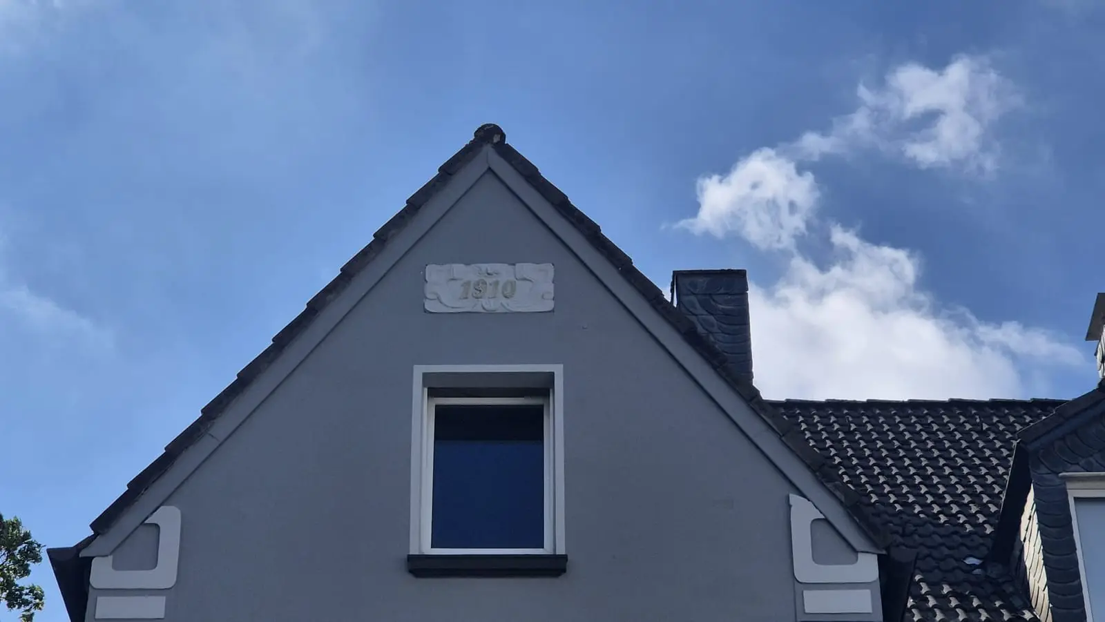 Giebel mit Stuckkartusche „1910" vor blauem Himmel