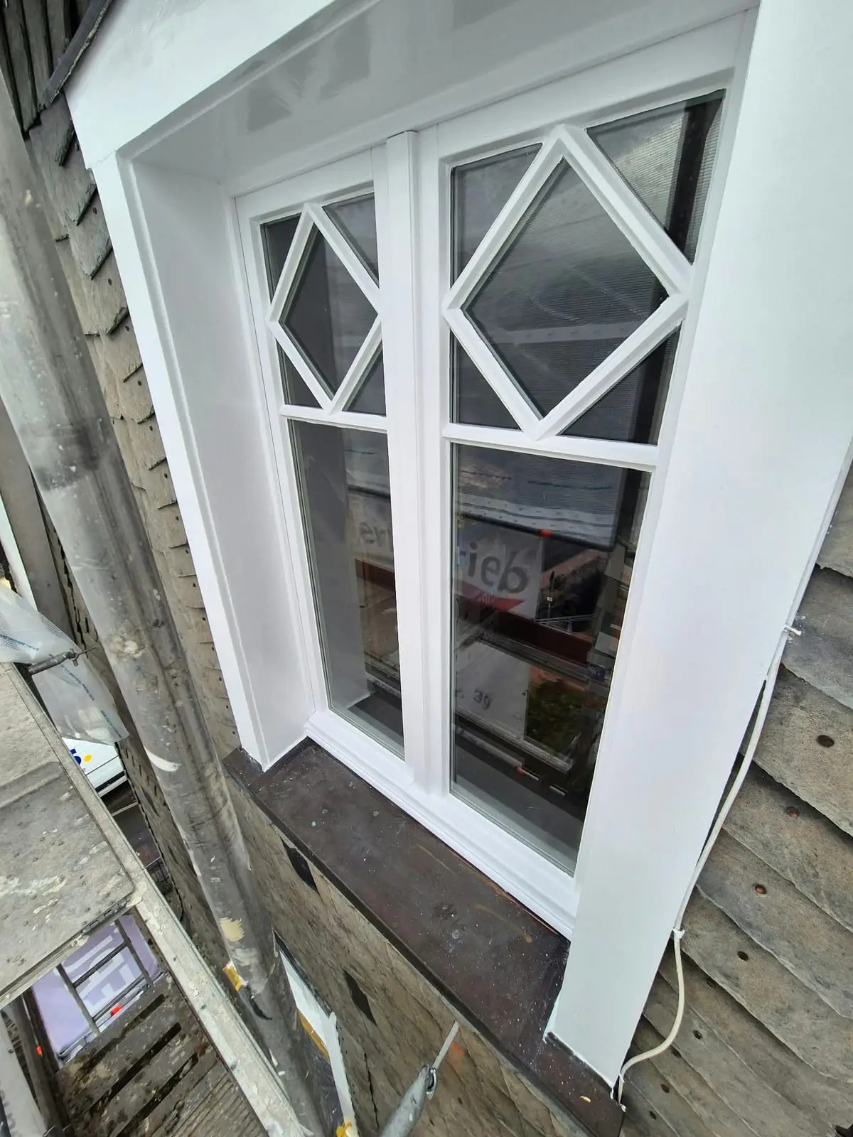 Frisch weiß lackiertes Sprossenfenster mit Rautenmuster in einer Schieferfassade