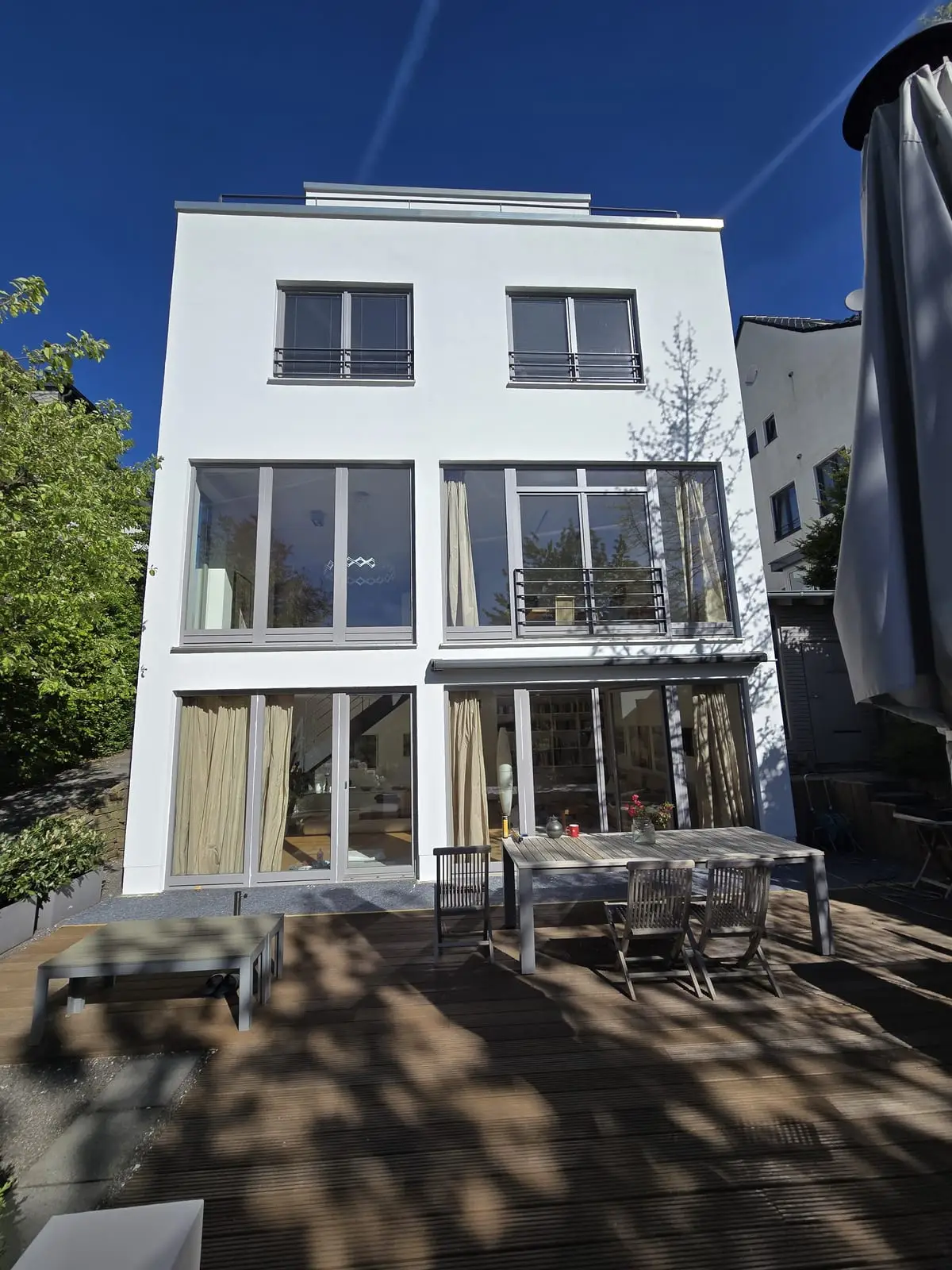 Die fertige weiße Gartenfassade des Stadthauses mit Holzterrasse