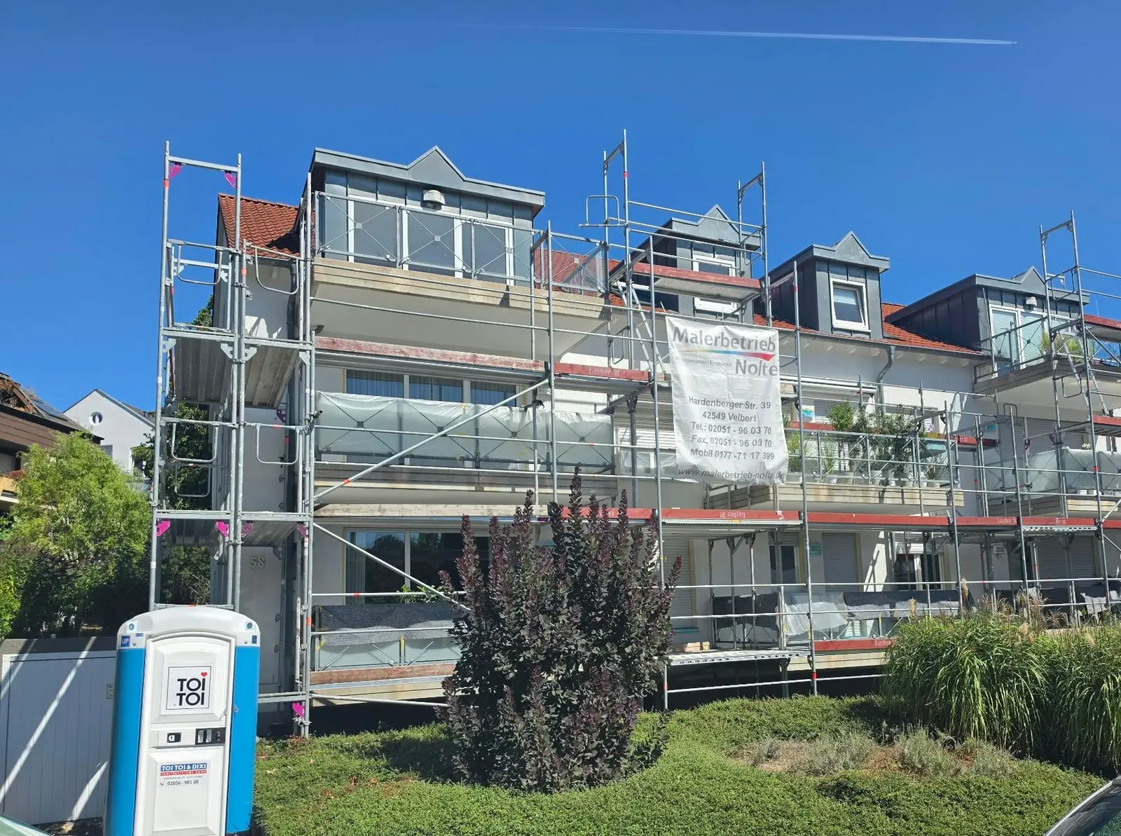 Das Mehrfamilienhaus komplett eingerüstet, Balkone mit Folie geschützt, Nolte-Banner am Gerüst